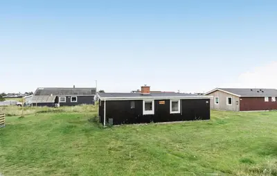 a black house in a field with houses in the background at 2 Bedroom Nice Home In Thisted in Thisted