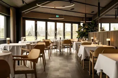 a restaurant with white tables and chairs and windows at Skønt Sommerhus Golfhytte midt i skønne omgivelser in Gatten