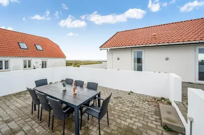 a patio with a wooden table and chairs at Pool And Activity House With A 180-Degree View Of The North Sea, Located At Lild Strand in Frøstrup