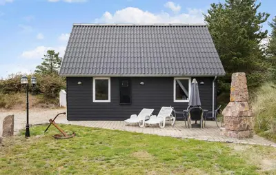 a black house with chairs and an umbrella on a deck at Gorgeous Home In Blokhus With Sauna in Blokhus