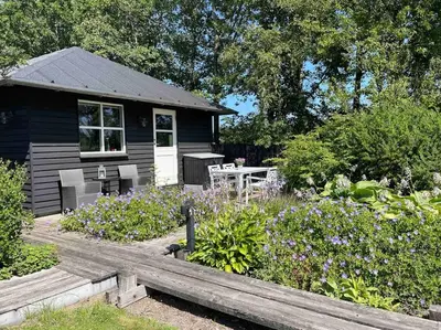 a black house with a table and chairs in a garden at Aneks i rolige omgivelser-adgang til pool og sauna in Avlum
