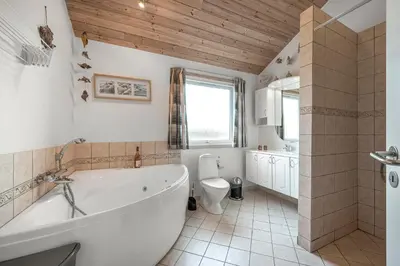 a bathroom with a white tub and a toilet at Holiday Home With Spa And Sauna, Just 200 Meters From The North Sea in Frøstrup