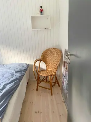 a wicker chair sitting next to a bed in a room at A Gem In The Woods Close To The North Sea in Rødhus