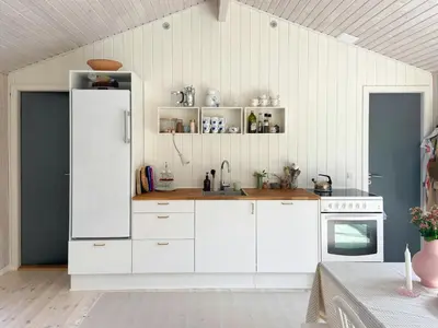 a kitchen with white cabinets and a white refrigerator at A Gem In The Woods Close To The North Sea in Rødhus