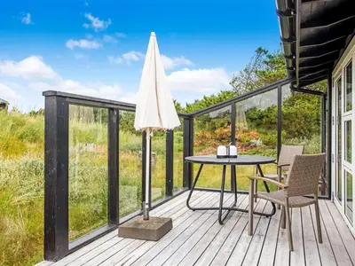 a deck with a table and chairs and an umbrella at Holiday Home Cate - 900m from the sea by Interhome in Saltum
