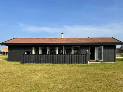 a black house with a red roof in a field at Architect-Designed Summer House In Agger in Vestervig