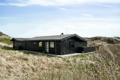 a black house in the middle of a field at 70'S Style Summerhouse Near Løkken in Løkken