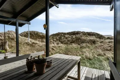 a wooden porch with potted plants and a table on a beach at 70'S Style Summerhouse Near Løkken in Løkken
