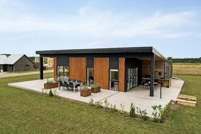 a small house with a wooden deck in a field at Modern Light House With Terrace Near The Fjord in Løgstrup