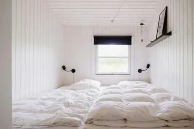 a large white bed in a white room with a window at Bright And Lovely Summerhouse In Løkken in Løkken