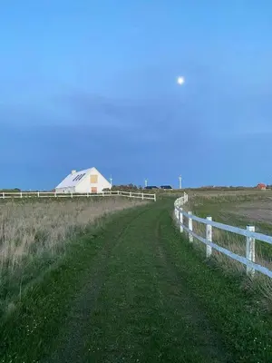 a white fence in a field with a white barn at Renovated Farmhouse In Architectural Style in Lemvig