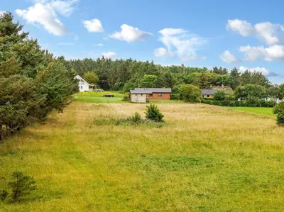 a field with a house and trees in the background at Lovely Holiday Home, Renovated In 2024, Located In Hanstholm By The North Sea in Hanstholm