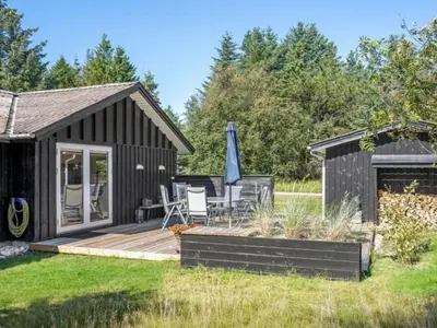 a black cottage with a deck and an umbrella at Holiday Home Quiana - 2km from the sea by Interhome in Pandrup