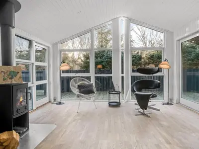 a living room with a fireplace and chairs and windows at Holiday Home Baldo - 800m from the sea by Interhome in Blokhus