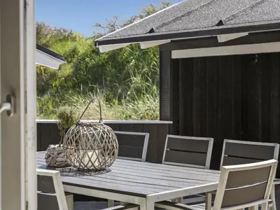 a wooden table with chairs and a basket on a patio at Holiday Home Erma - 125m from the sea by Interhome in Saltum