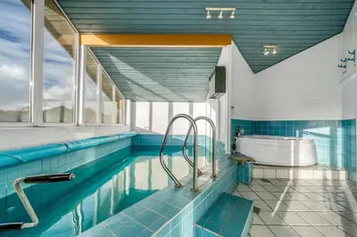 a bathroom with a swimming pool with blue tiles at Lovely Holiday Home With Pool, Spa And Sauna, Only 200 Meters From The North Sea in Harboør