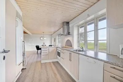 a kitchen with white cabinets and a dining room with a table at Jørgen's Feriehus in Lemvig