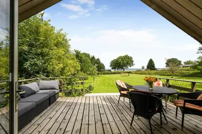 a deck with a couch and a table and chairs at Charming Summerhouse With A View Of The Limfjord in Roslev