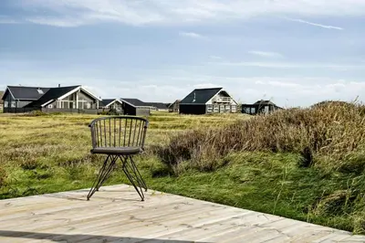 a chair sitting on a boardwalk in a field with houses at Minimalist Coziness By The Wild North Sea in Harboør