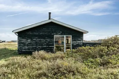 a black building with a window in a field at Minimalist Coziness By The Wild North Sea in Harboør