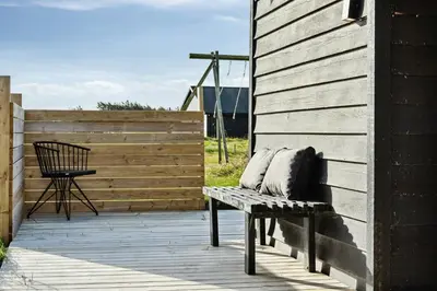 a bench sitting on a deck next to a wooden wall at Minimalist Coziness By The Wild North Sea in Harboør