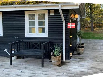 a black house with a bench on a patio at Family House At Kryle Klit Near Wild Nature in Blokhus