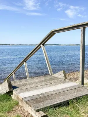 a wooden bench sitting next to a body of water at Historic House With Fjord View On Venø in Vemb