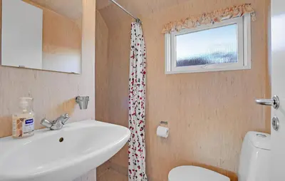 a bathroom with a sink and a toilet and a window at Toftum Bjerge Camping & Cottages in Humlum