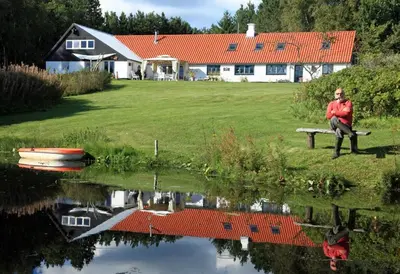 a woman sitting on a bench next to a lake at Alt det bedste mellem hav og fjord - en hel bolig in Brovst