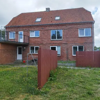 a brick house with a red fence in front of it at Hyggelig lejlighed i stille by in Vemb