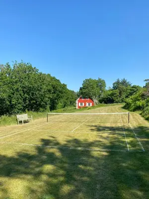 a tennis court with a red house in the background at Romance And Sea View At Havbakken in Fjerritslev