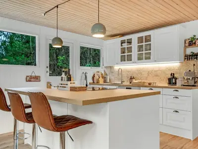 a kitchen with white cabinets and a wooden ceiling at Holiday Home Hansa - 3km from the sea by Interhome in Blokhus