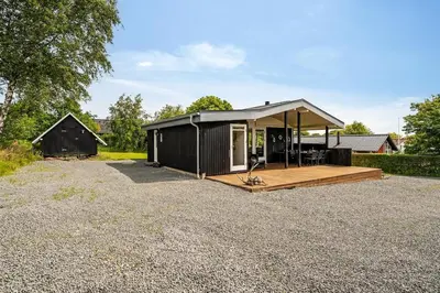 a black shed with a porch and a deck at Charming little cottage in Roslev