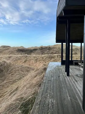 a wooden deck with a bench on top of a field at Wooden House In The Dunes Close To The Sea in Pandrup