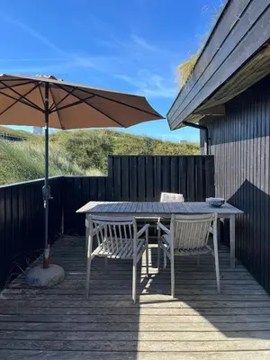 a table and two chairs and an umbrella on a deck at Wooden House In The Dunes Close To The Sea in Pandrup