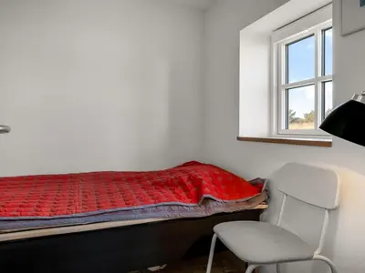 a bedroom with a bed and a chair and a window at Holiday Home Amina - 200m from the sea by Interhome in Blokhus