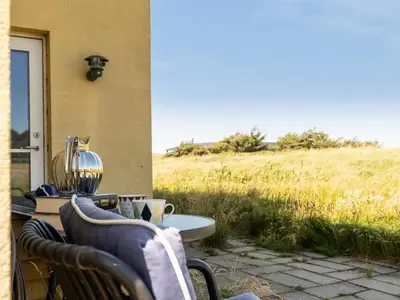 a patio with a table and chairs and a field at Holiday Home Amina - 200m from the sea by Interhome in Blokhus