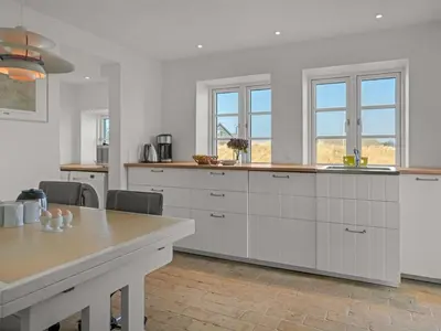 a kitchen with white cabinets and a table and windows at Holiday Home Amina - 200m from the sea by Interhome in Blokhus