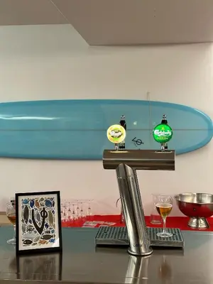 a counter with wine glasses and a surfboard on a wall at VØ Drop Inn in Nørre Vorupør