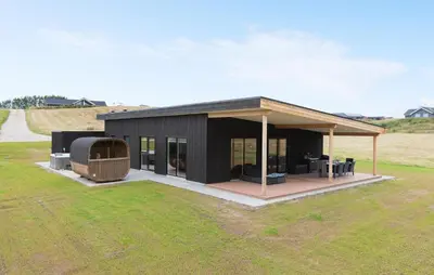 a black house with a deck in a field at Lovely Home In Spøttrup With Sauna in Spottrup
