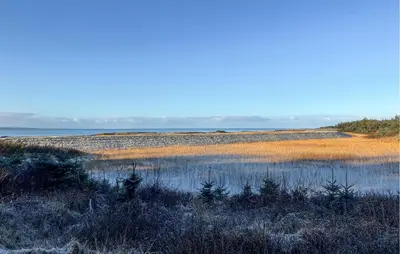 a field with a body of water and some grass at Beach Front Home In Thyholm With Sauna in Thyholm