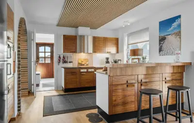 a kitchen with wooden cabinets and bar stools at Amazing Home In Thyborøn With Sauna in Thyborøn