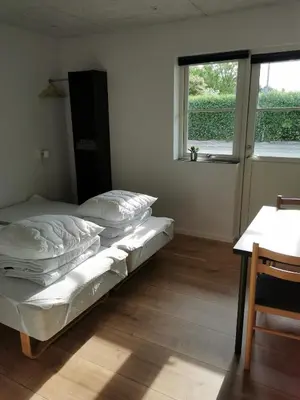 a bedroom with a bed and a table and a window at Ferielejlighed in Nibe