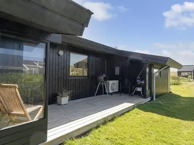 a black house with a wooden deck in the grass at Holiday Home Waghn - 250m from the sea by Interhome in Harboør