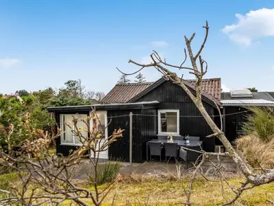 a black house with a table in front of it at Holiday Home Godja - 1km from the sea by Interhome in Blokhus
