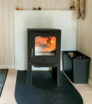 a stove sitting in a room with a trash can at Forest Cabin With Panoramic View Near Blokhus in Blokhus