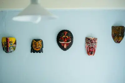 a group of masks hanging on a wall at Cut Branches, Make Fire And Gaze At Treetops in Nykøbing Mors