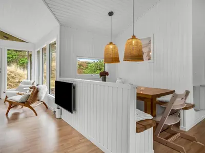 a white dining room with a table and a television at Holiday Home Gundborg - 200m from the sea by Interhome in Saltum