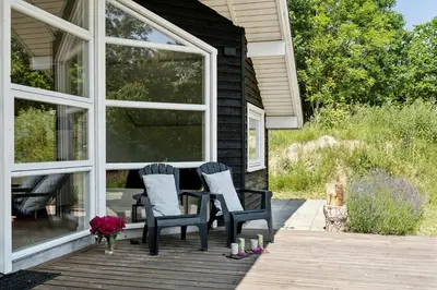 a porch with two chairs and a table with flowers at Forest House With Stream By Hjarbæk Fjord in Højslev