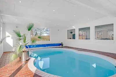 a large swimming pool in a white room with a blue swimming poolvisor at Holiday Home With Pool And Spa Close To The Limfjord in Roslev